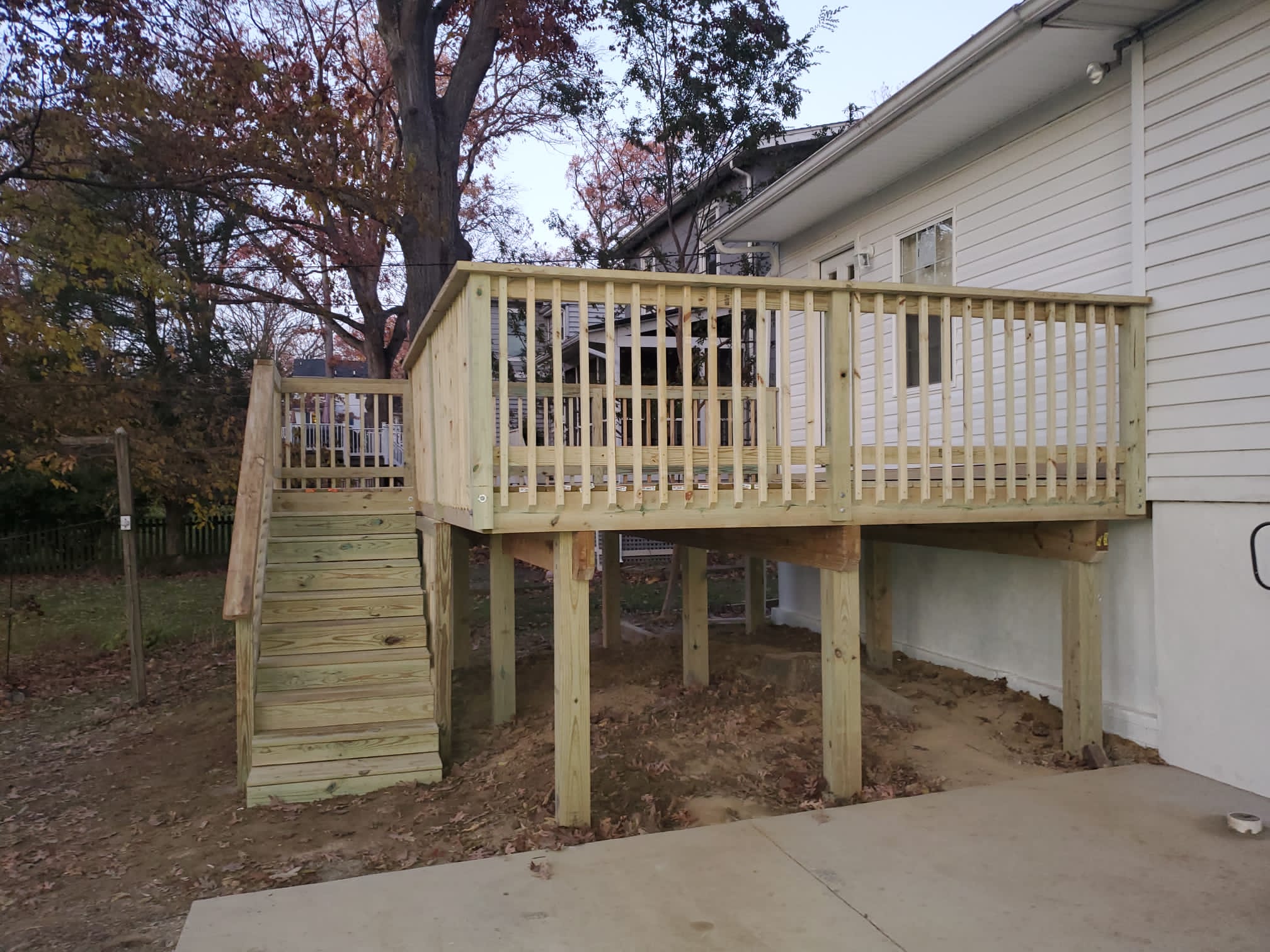 A newly built wooden deck with stairs, attached to a light-colored house, in a backyard with trees.
