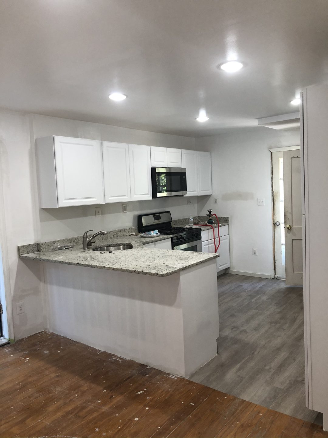 Modern kitchen with white cabinets, granite countertops, and stainless steel appliances, next to wood and tile floors.