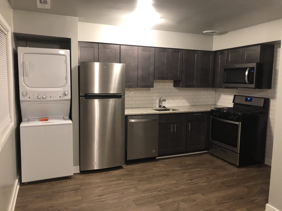 Modern kitchen with stainless steel appliances, dark cabinets, and a stacked washer-dryer in the corner.