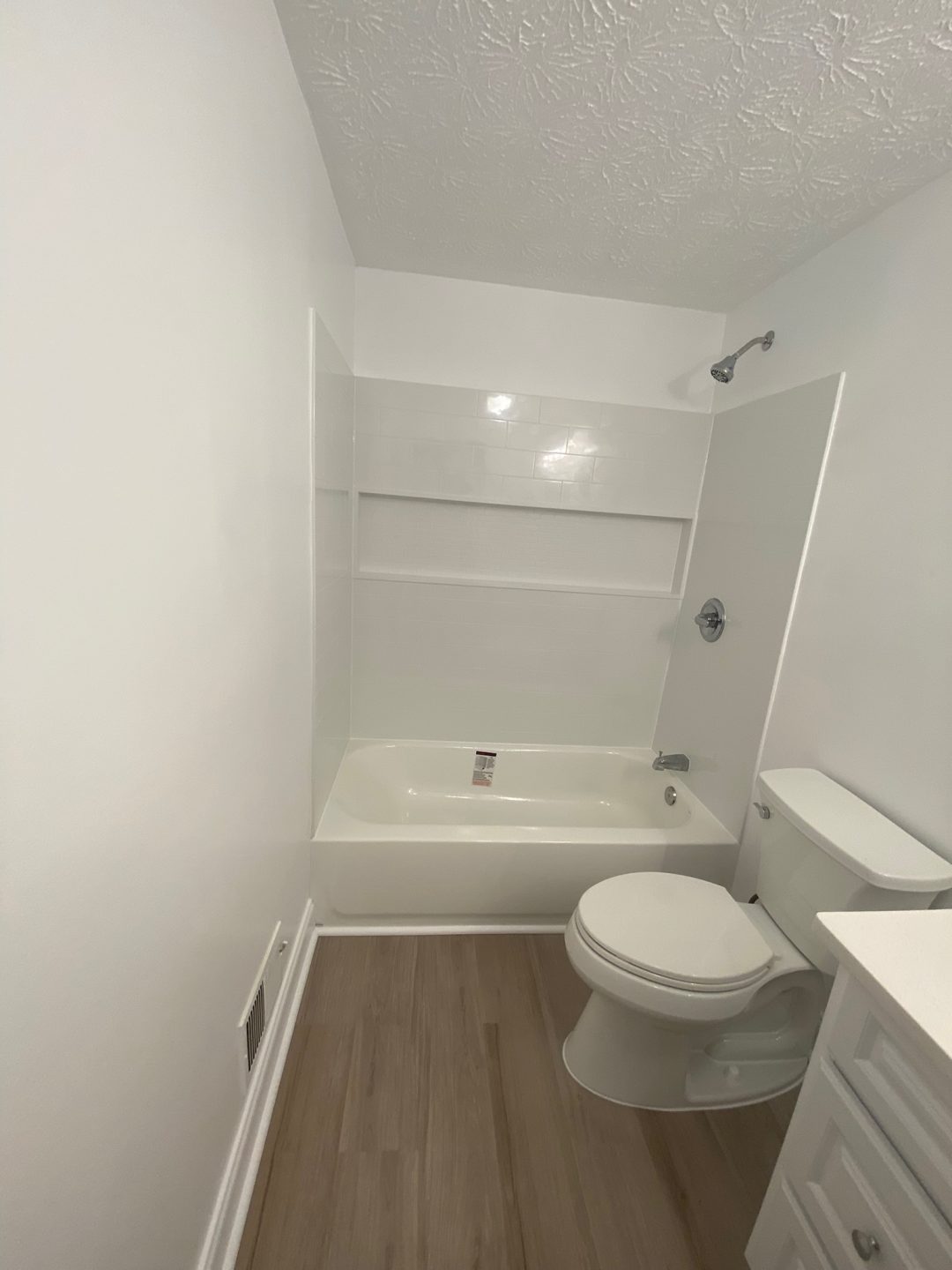 Small bathroom with white walls, a bathtub-shower combo, toilet, and wood-look flooring.