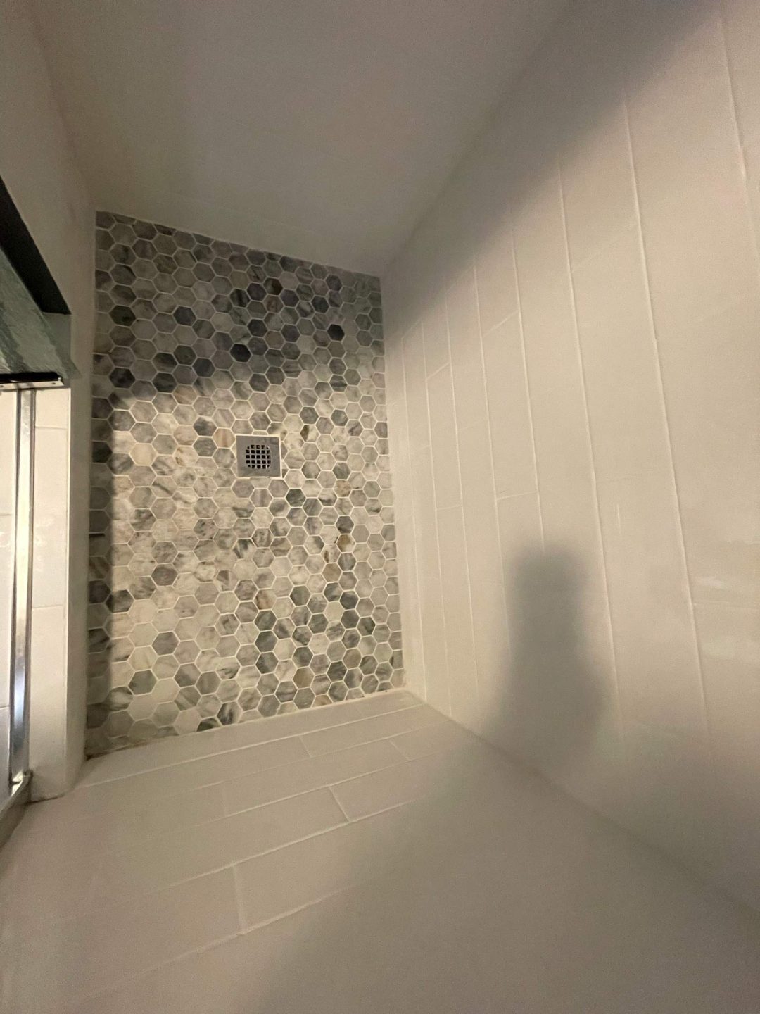 Shower with white rectangular wall tiles and a back wall of gray hexagonal tiles with a square drain.