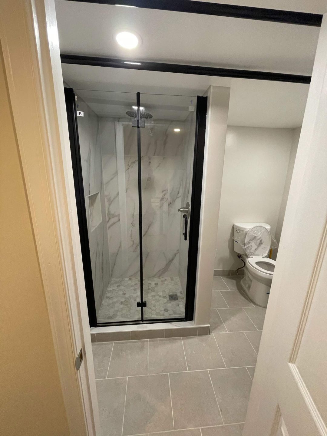 Modern bathroom with a glass shower enclosure and a toilet, featuring gray tile flooring.