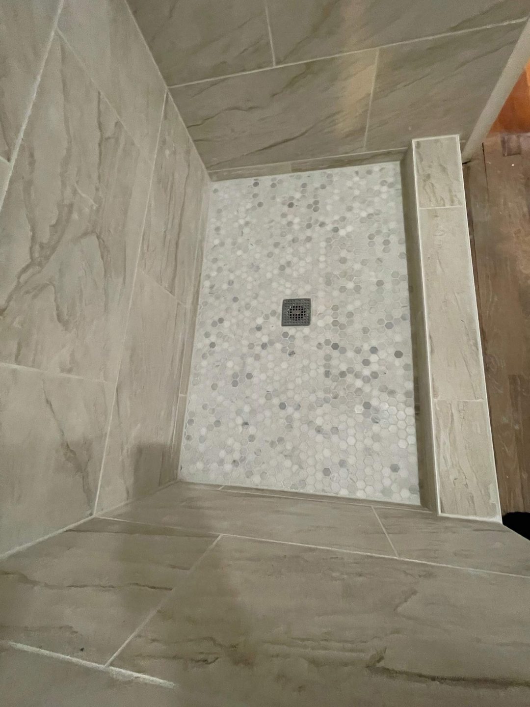 Overhead view of a tiled shower floor with hexagonal white tiles and a square drain in the center.