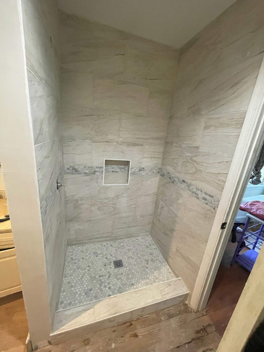 Newly tiled walk-in shower with a built-in niche and mosaic tile floor, no fixtures installed yet.