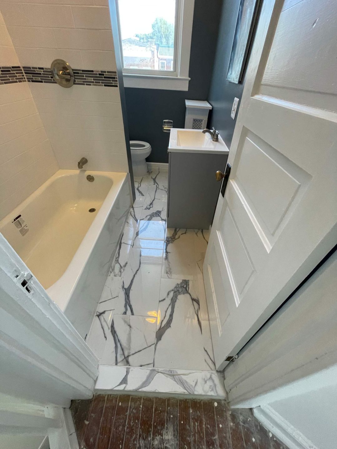 Small bathroom with a bathtub, toilet, sink, and gray marble tile floor, viewed from the doorway.