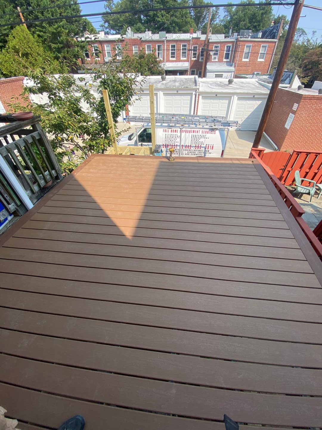 A newly finished brown wooden deck overlooks a small yard and a row of garages in a city neighborhood.