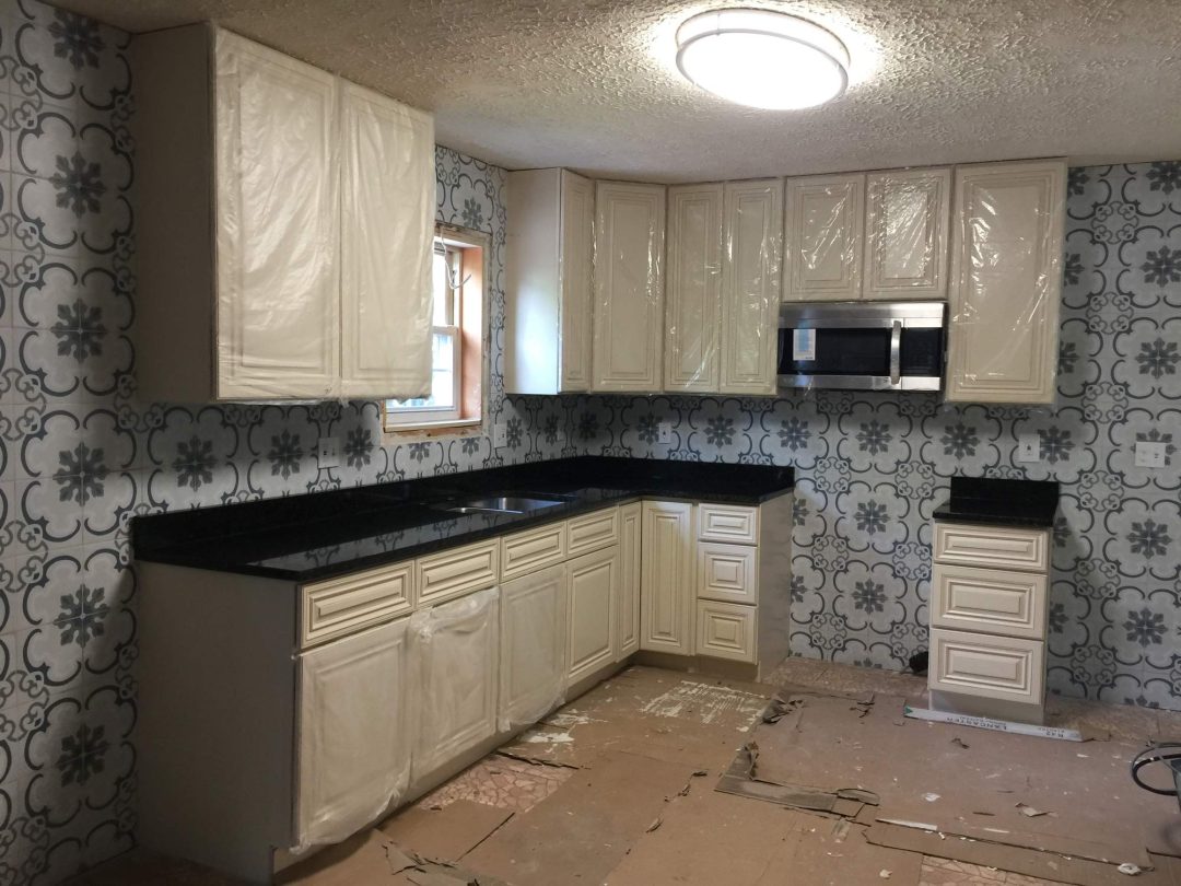Unfinished kitchen with cream cabinets, black countertops, floral wallpaper, and protective plastic on doors.