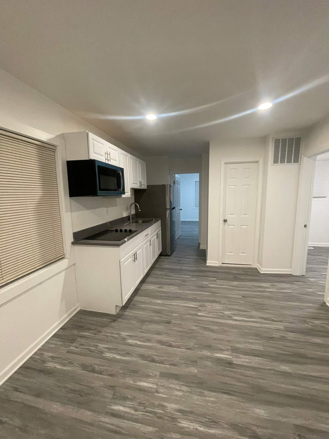 Modern kitchen with white cabinets, gray flooring, microwave, stove, fridge, and bright ceiling lights.