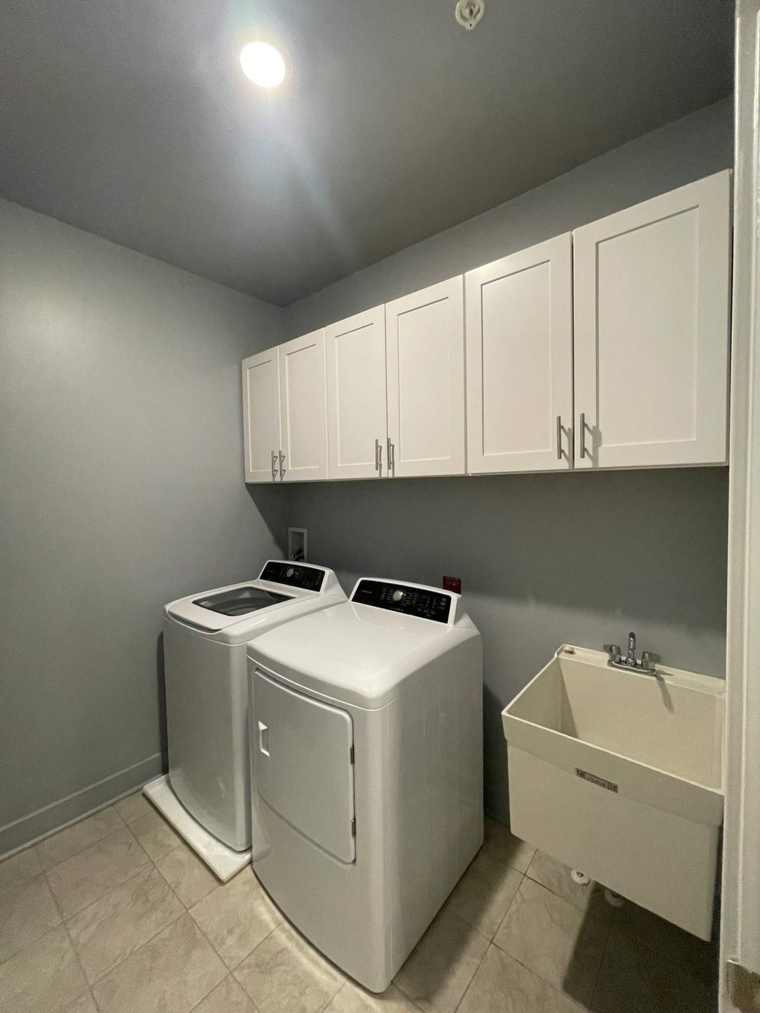 A laundry room with a washer, dryer, white cabinets, and a utility sink under bright lighting.