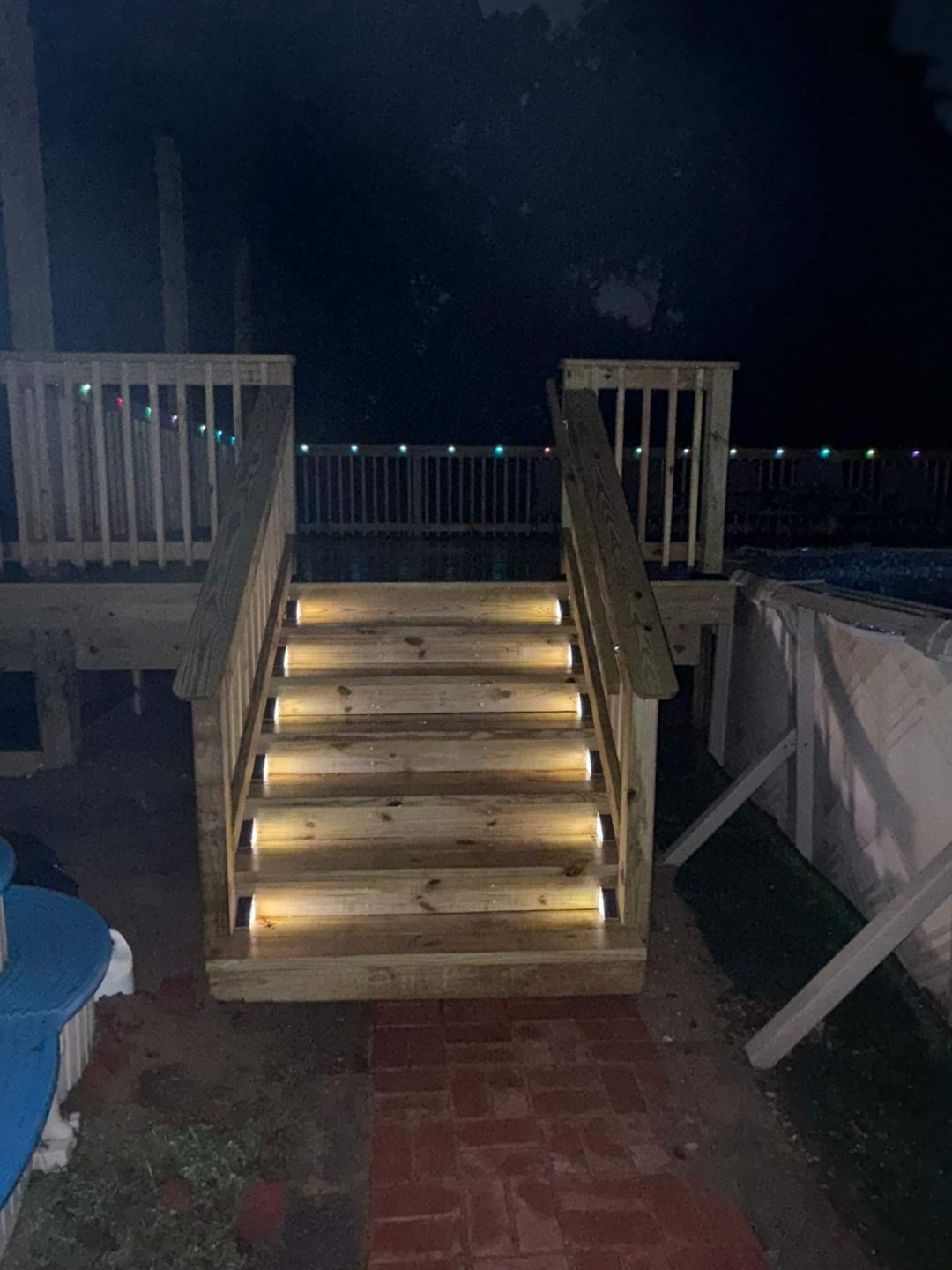 Wooden outdoor stairs with built-in lights at night, leading up to a deck with railings.