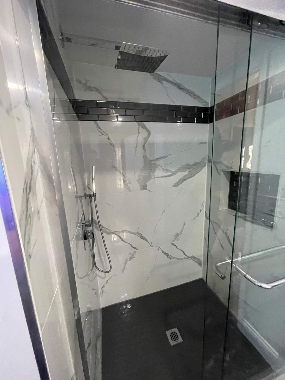 Modern shower with marble-patterned walls, a rainfall showerhead, and glass doors with a metal handle.