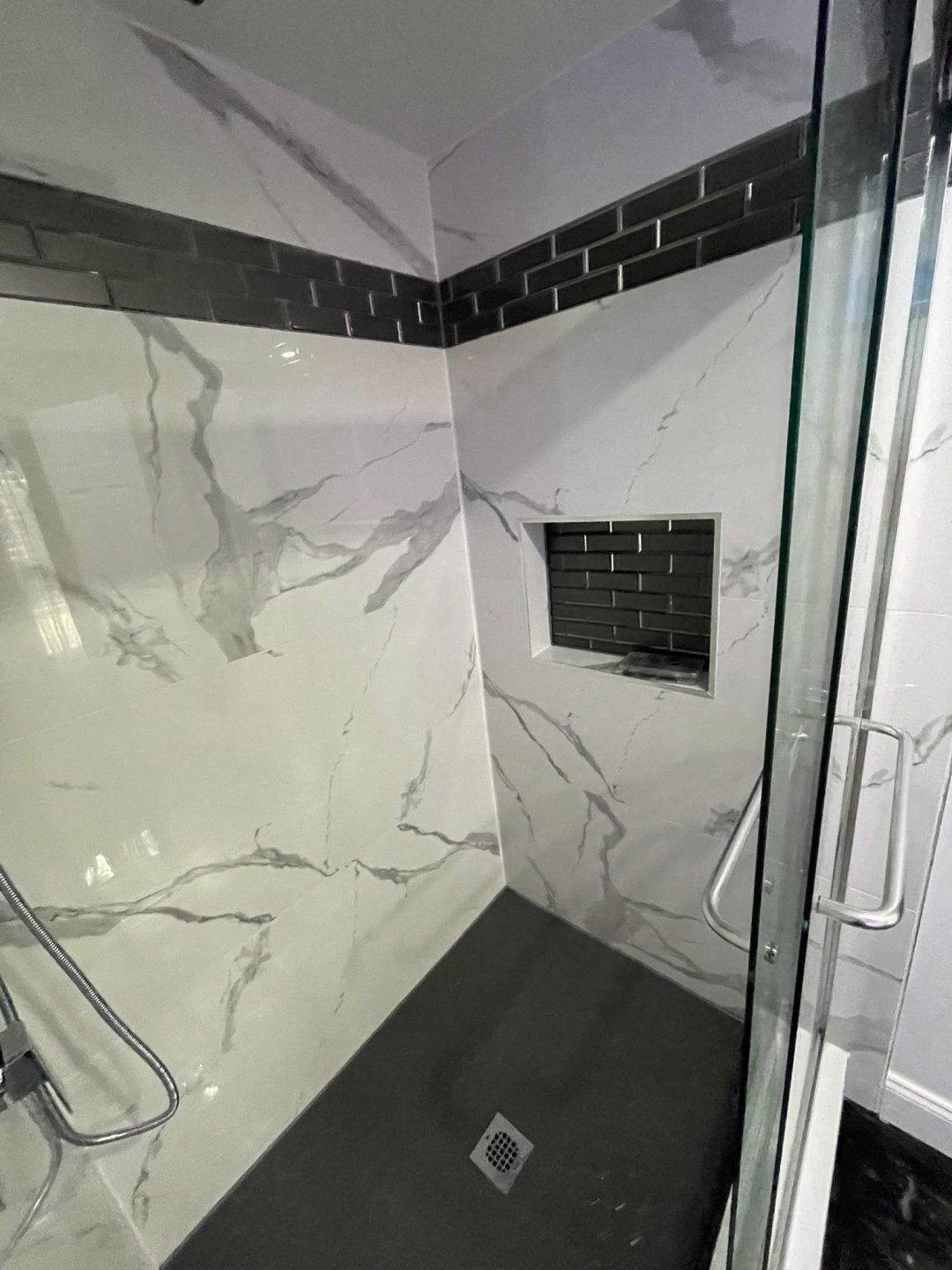 Modern shower with white marble-patterned walls, dark gray tiles, and a built-in shelf with matching tile.