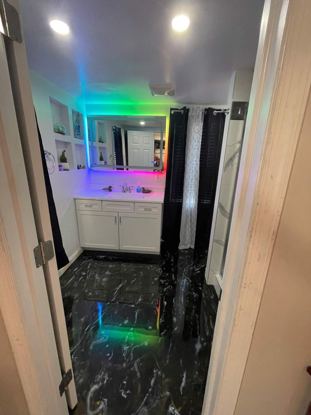 Modern bathroom with black marble floor and a vanity mirror lit by colorful LED lights.