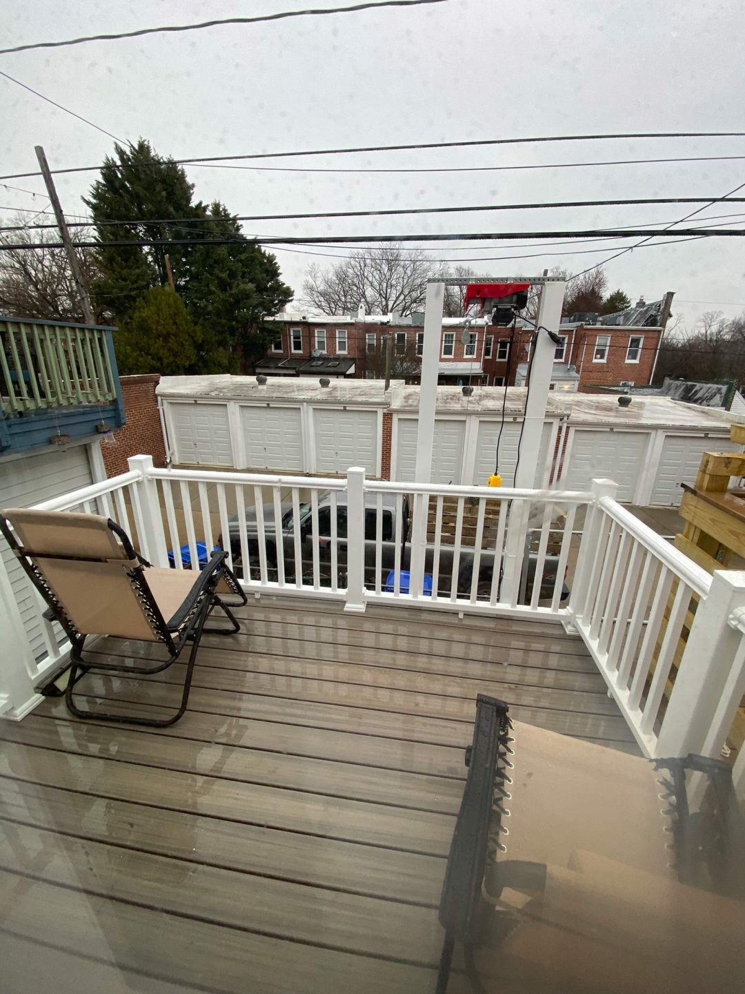 A small patio with two lounge chairs, white railing, and a view of houses, trucks, and power lines.