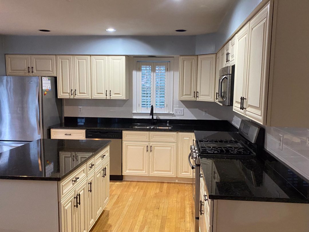 Modern kitchen with cream cabinets, black countertops, stainless steel appliances, and a central island.