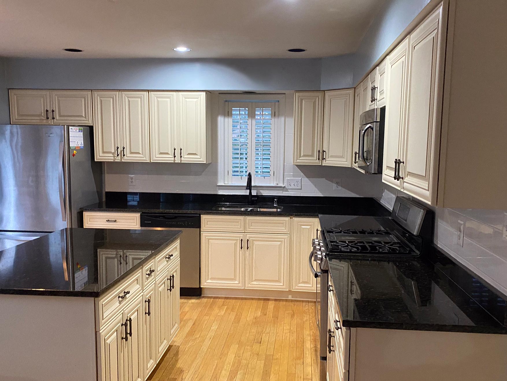 Modern kitchen with white cabinets, black countertops, stainless steel appliances, and wood flooring.