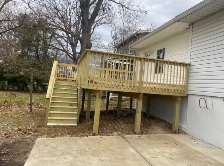 A newly built wooden deck with stairs attached to a white house, overlooking a concrete patio.