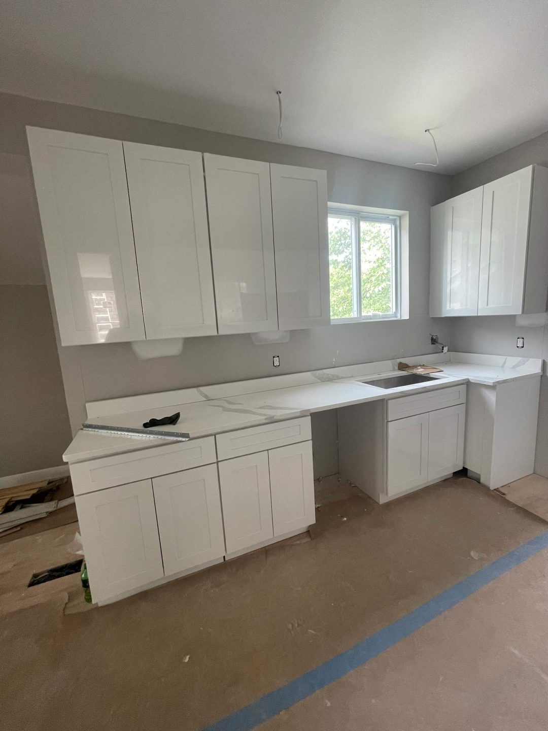 A kitchen under construction with white cabinets, no appliances, and an unfinished floor.