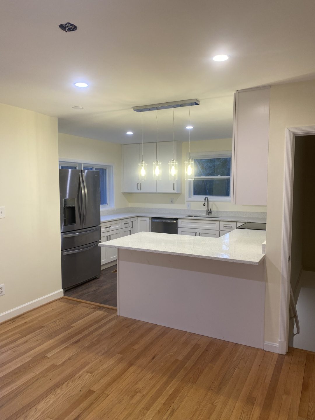Modern kitchen with white cabinets, stainless steel appliances, island, and hanging pendant lights.