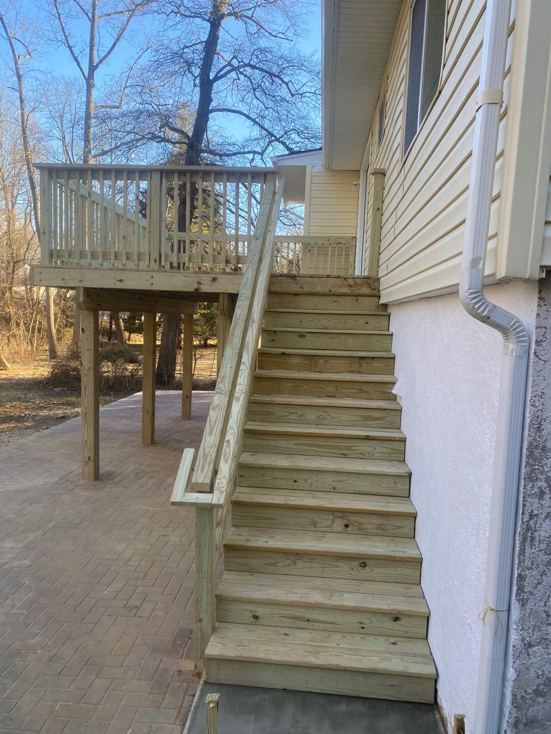 Wooden stairs lead up to a raised deck attached to a house, with trees visible in the background.