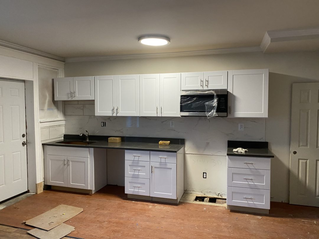 A partially finished kitchen with white cabinets, black countertops, and an installed microwave.
