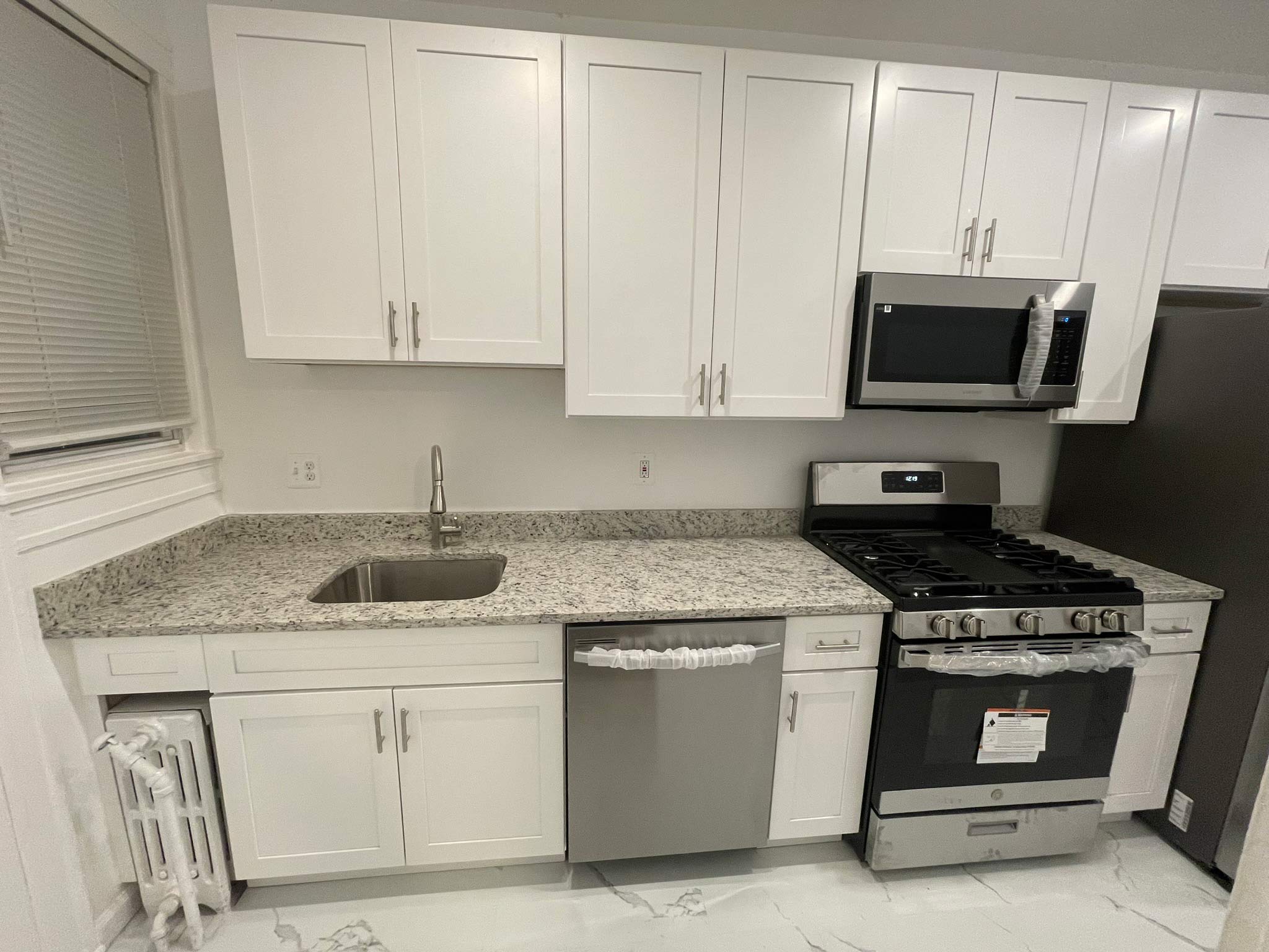 Modern kitchen with white cabinets, granite countertop, stainless steel appliances, and tile floor.
