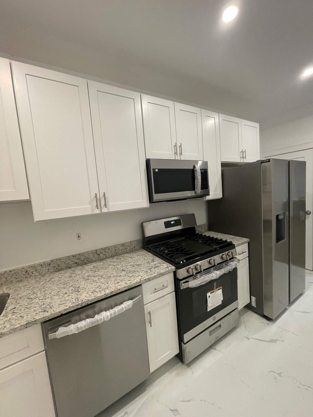 Modern kitchen with white cabinets, granite countertops, stainless steel appliances, and bright lighting.