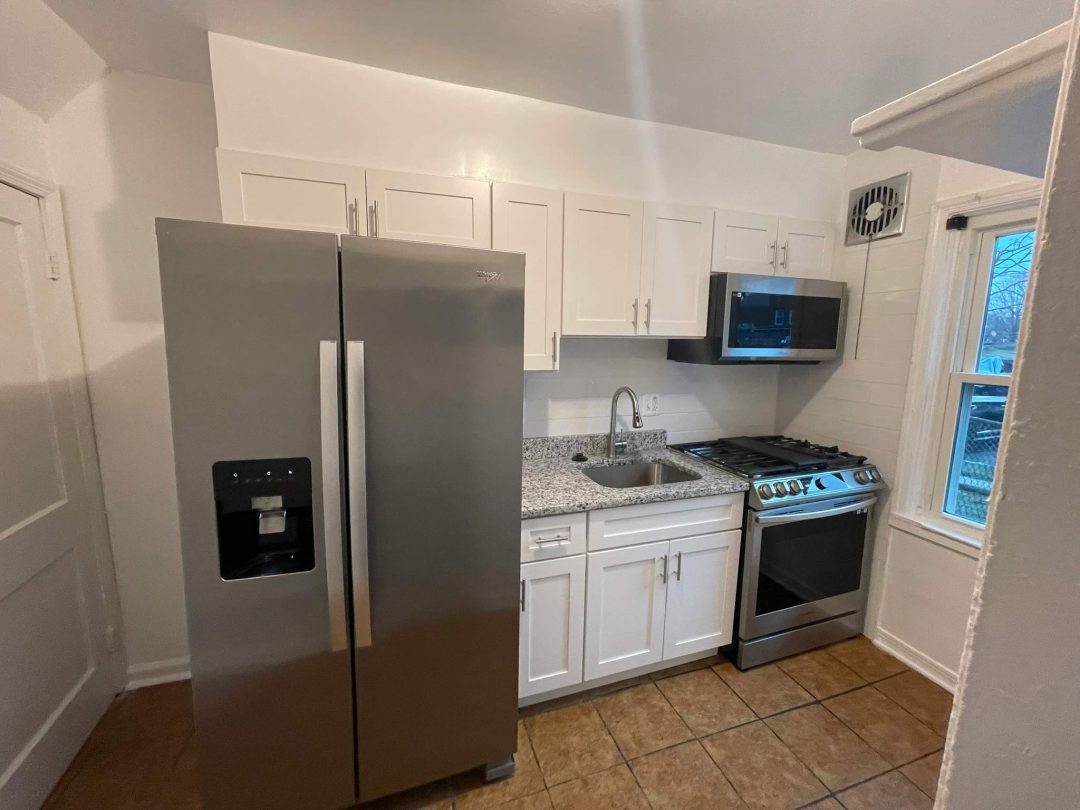 Modern kitchen with stainless steel appliances, white cabinets, granite countertops, and a tiled floor.