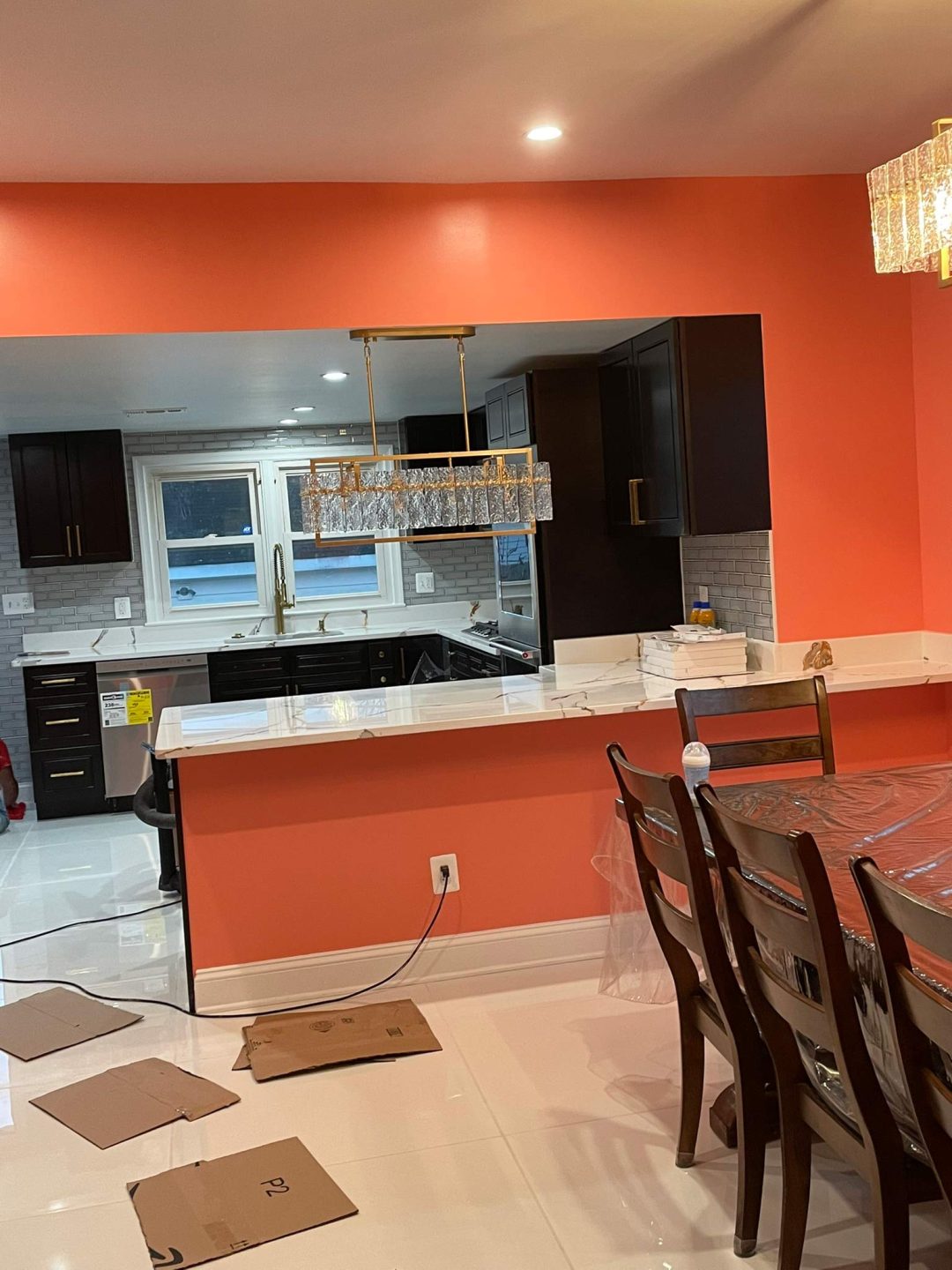 Modern kitchen and dining area with coral walls, dark cabinets, and crystal chandelier; some cardboard on the floor.