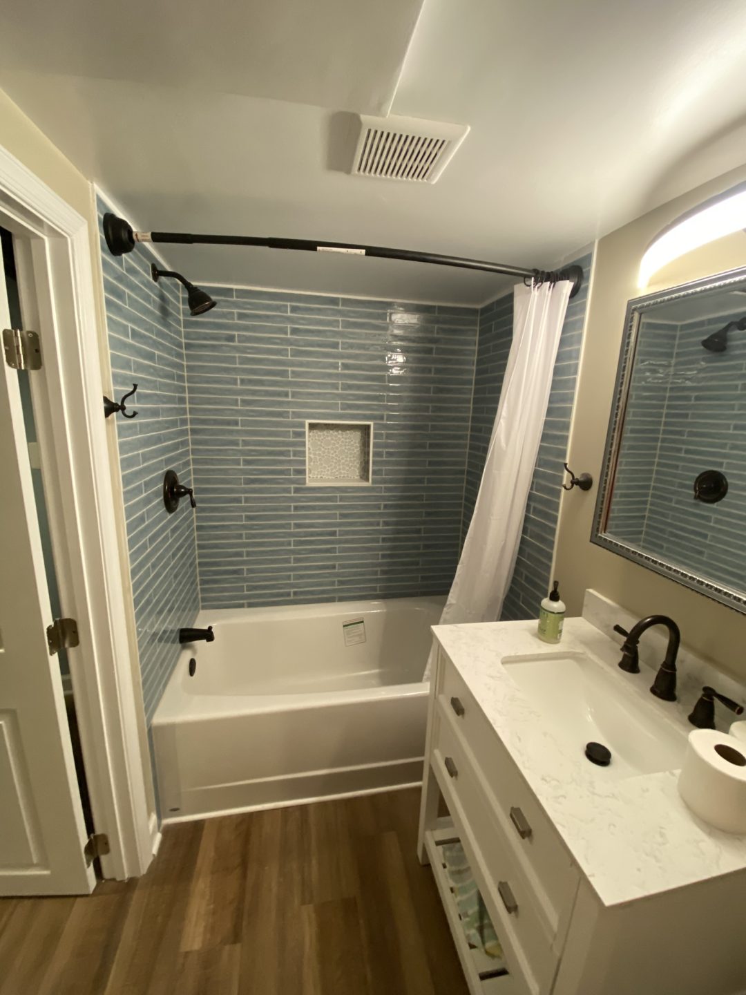 Modern bathroom with blue subway tile, white bathtub, white vanity, and wood-look floor.