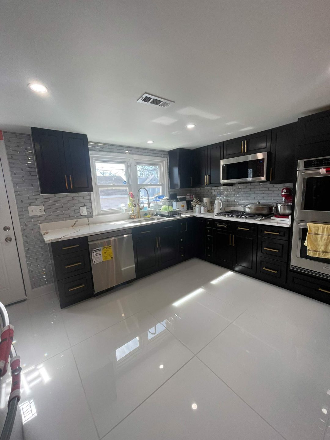 Modern kitchen with dark cabinets, white countertops, and stainless steel appliances, brightly lit by sunlight.