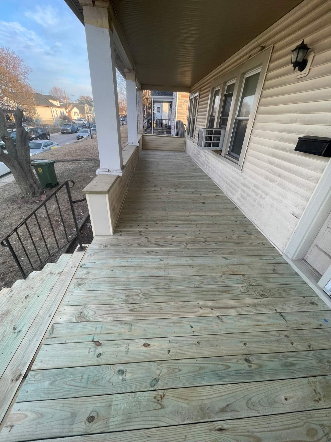 Wide-angle view of a clean, freshly built wooden porch attached to a beige house on a residential street.