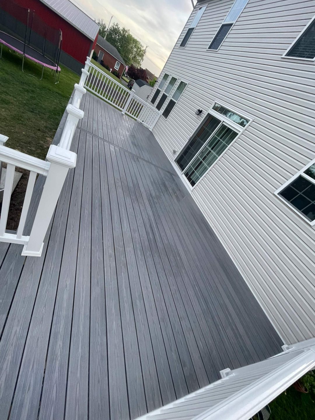 A gray backyard deck with white railings attached to a white house, viewed from one end.