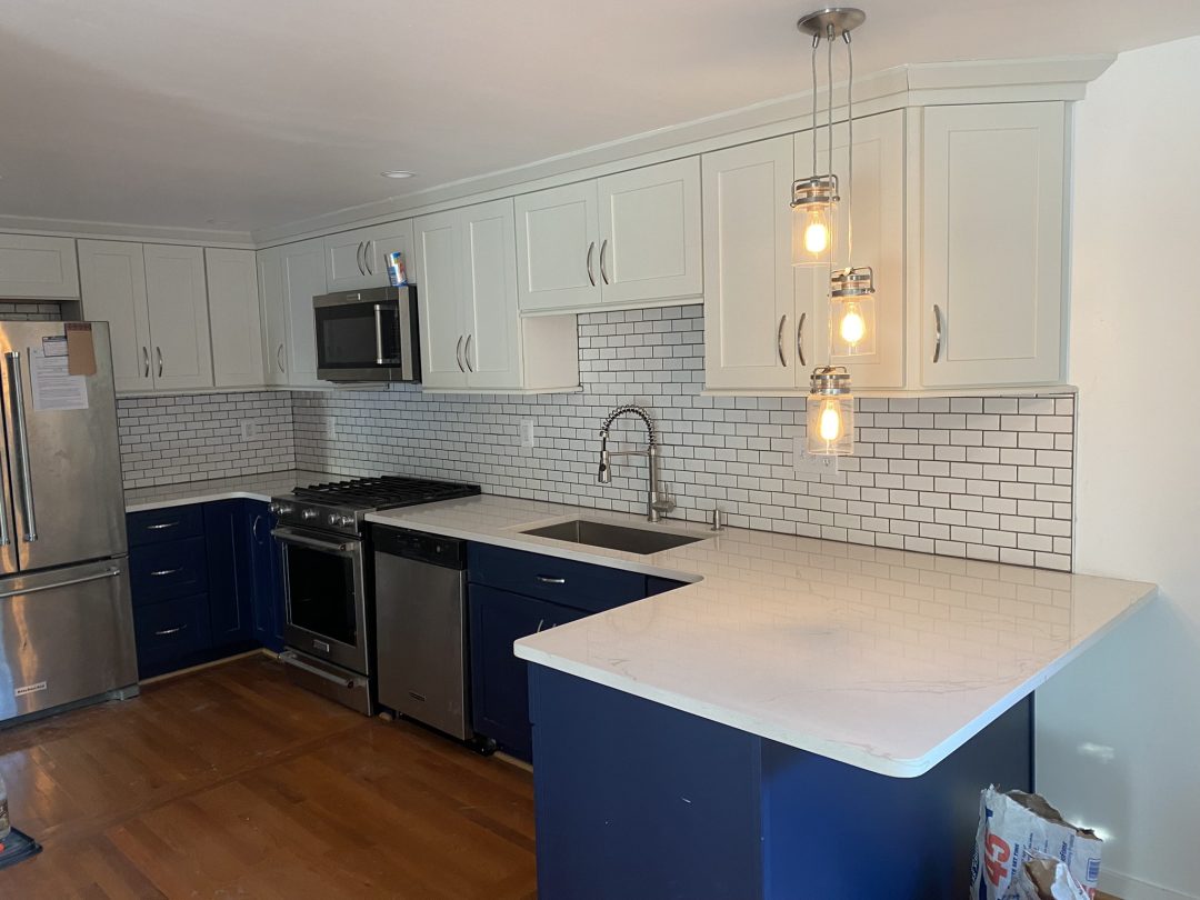Modern kitchen with white cabinets, blue lower cabinets, subway tile backsplash, and hanging pendant lights.