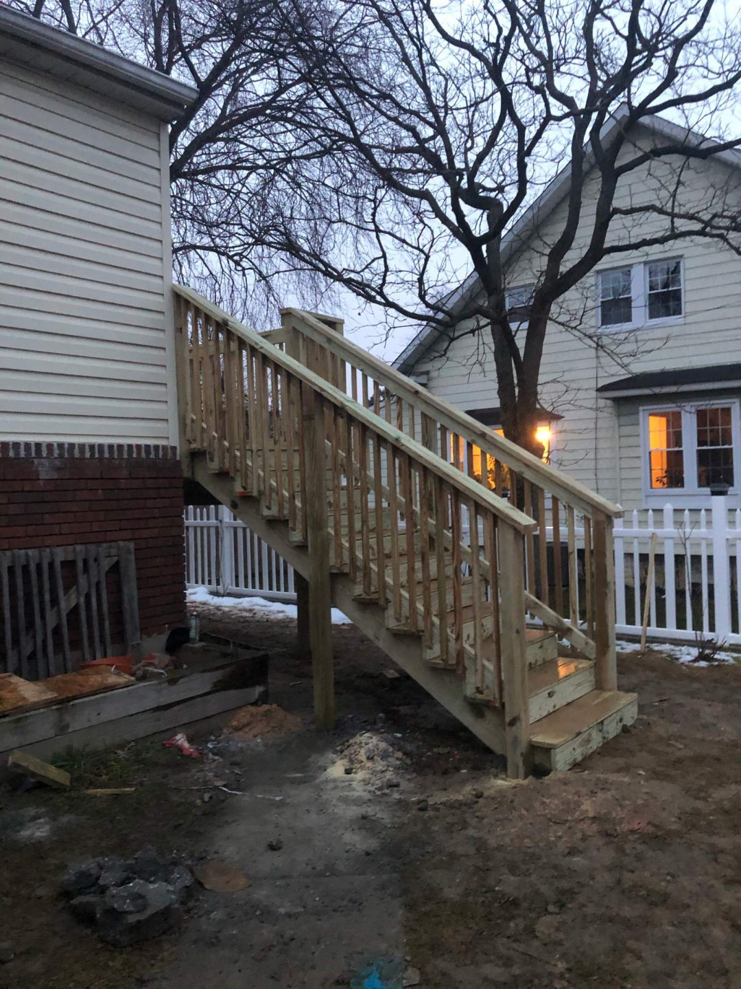 A newly built wooden staircase outside a house, leading to a second-story door, with a white fence nearby.
