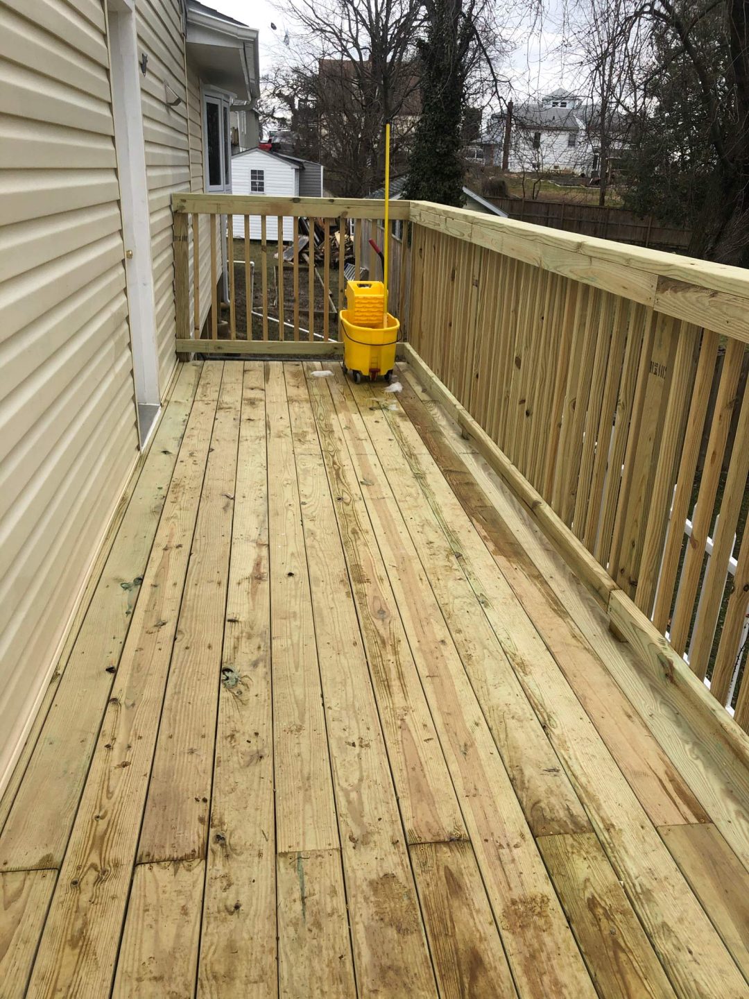 A wooden deck with a yellow mop bucket and mop near the railing on a cloudy day.