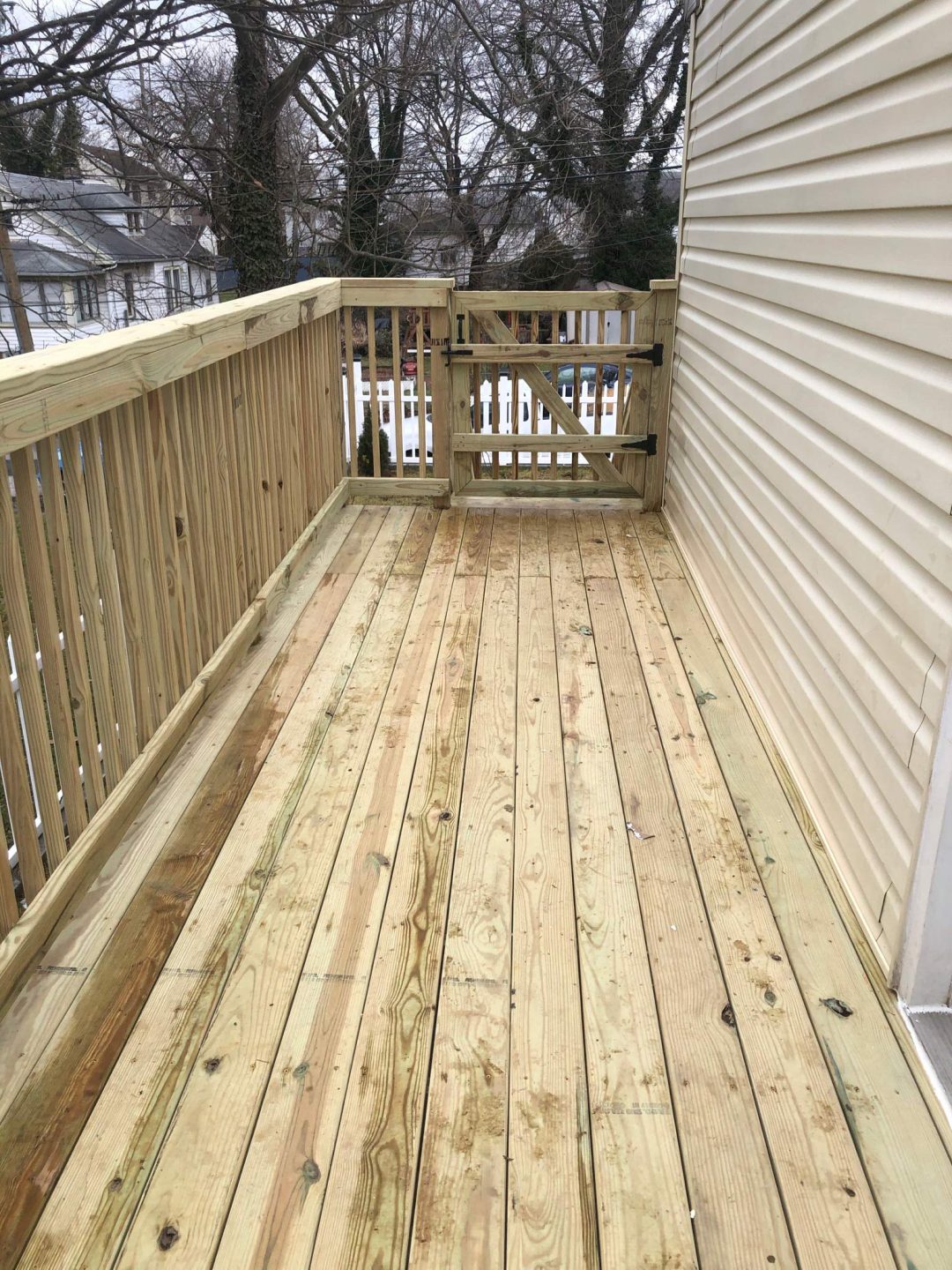 A newly built wooden balcony with railings and a gate, attached to the side of a house.