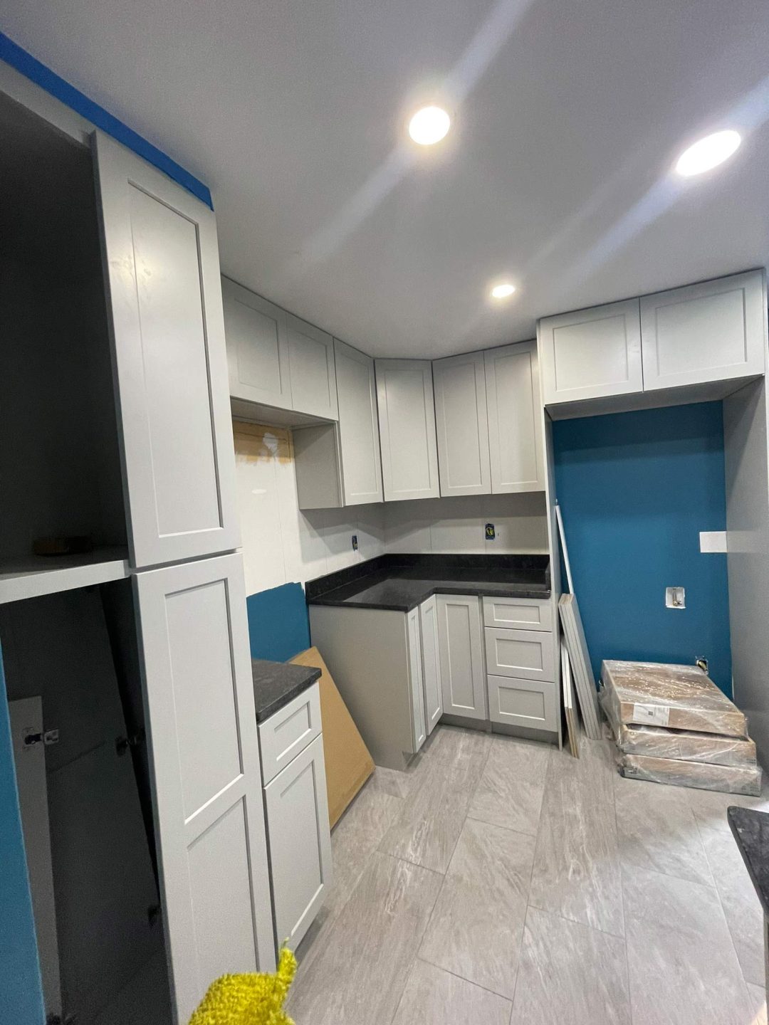 Modern kitchen under renovation with gray cabinets, blue walls, and tiles on the floor.