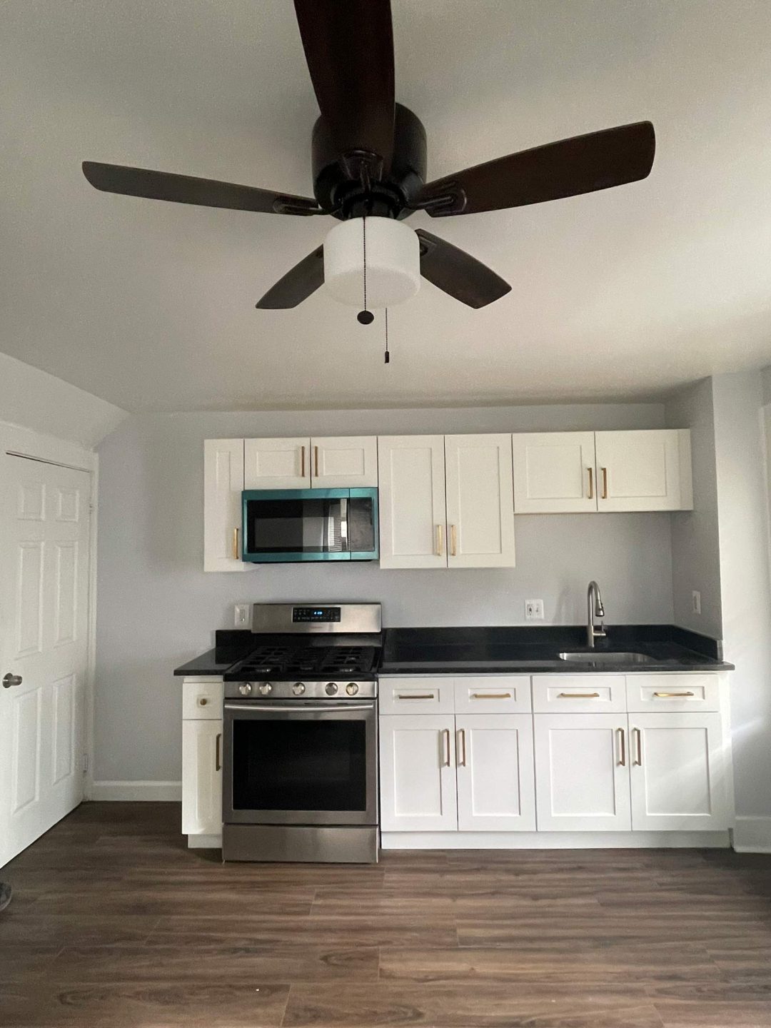 Modern kitchen with white cabinets, stainless steel appliances, and a ceiling fan with dark blades.