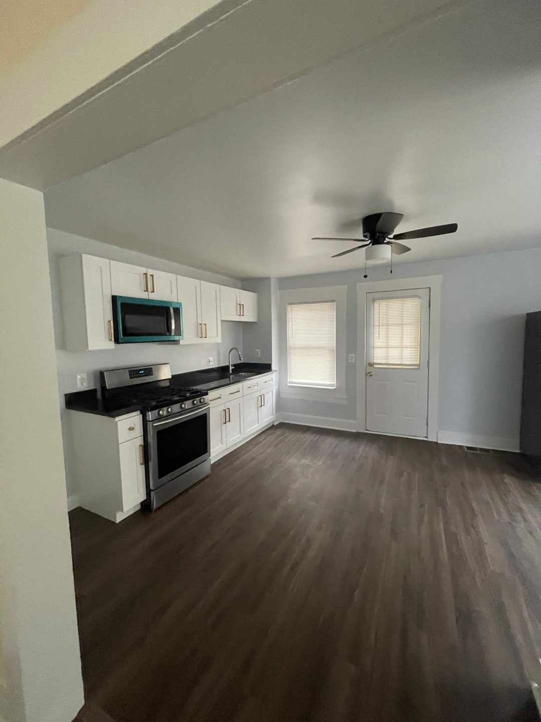 Modern kitchen with white cabinets, stainless appliances, dark countertops, wood floors, and a ceiling fan.