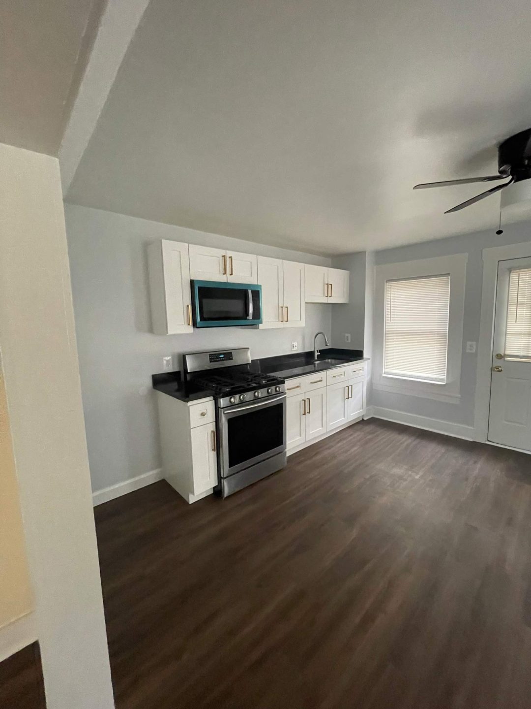 Modern kitchen with white cabinets, stainless steel appliances, and dark wood floors in a bright room.