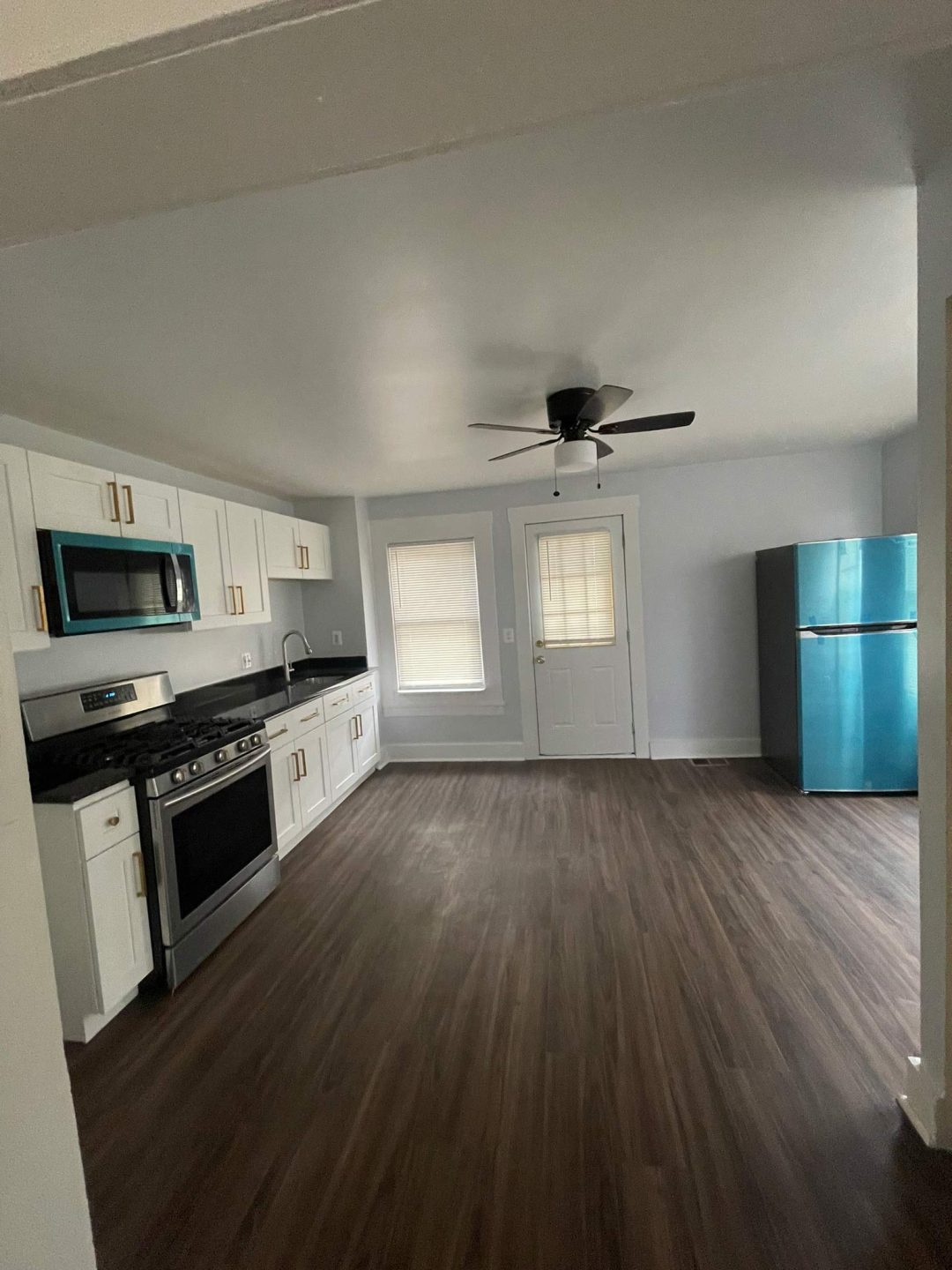 Modern kitchen with white cabinets, stainless steel appliances, blue fridge, and dark wood floors.