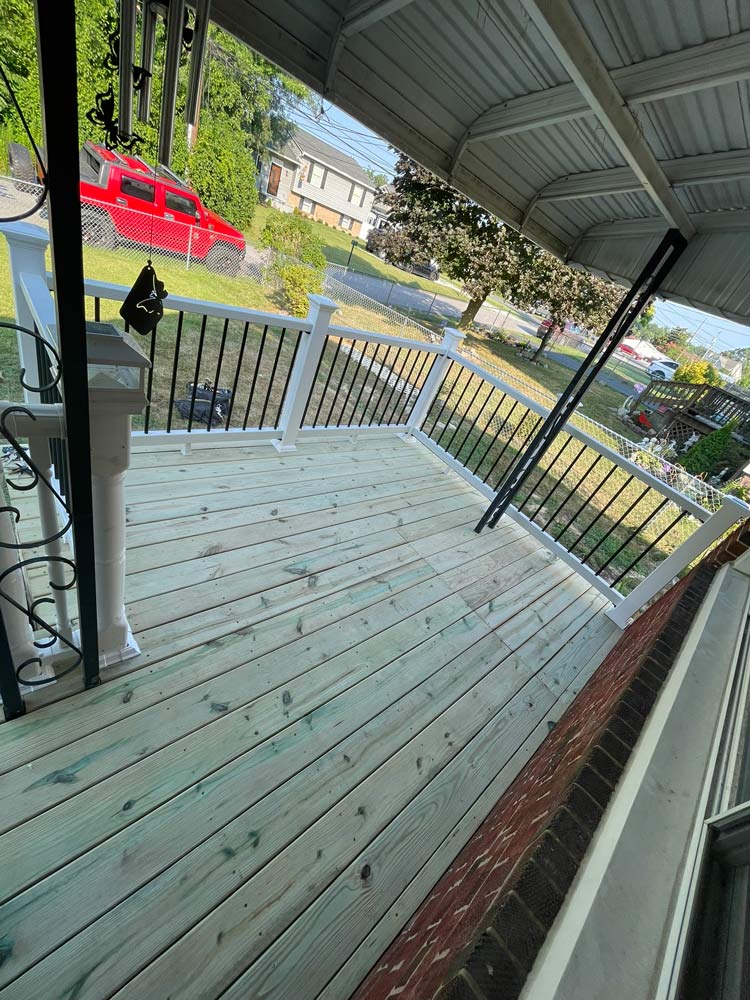 View of a freshly built wooden porch with black railings, overlooking a street with parked cars and houses.