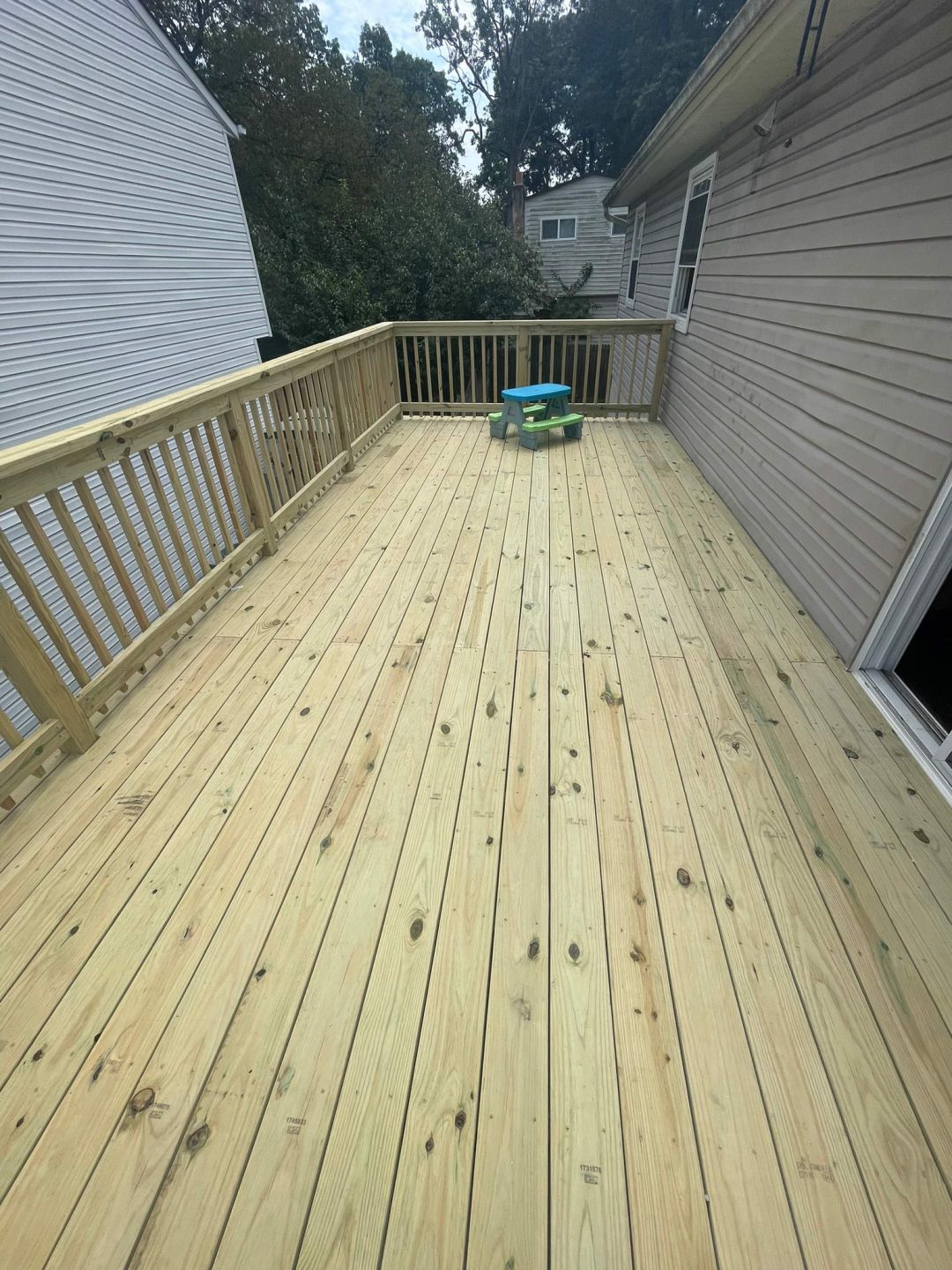 A spacious wooden deck with a small green and blue plastic chair, attached to a beige house.
