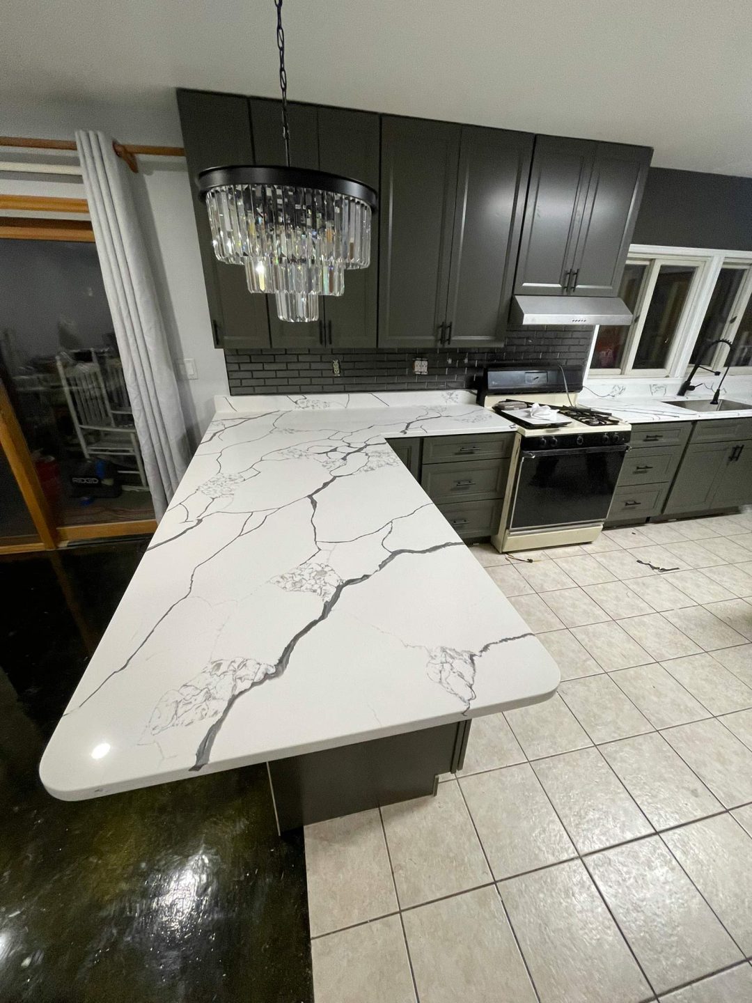 Modern kitchen with white marble-style countertops, dark cabinets, and a crystal chandelier above the island.