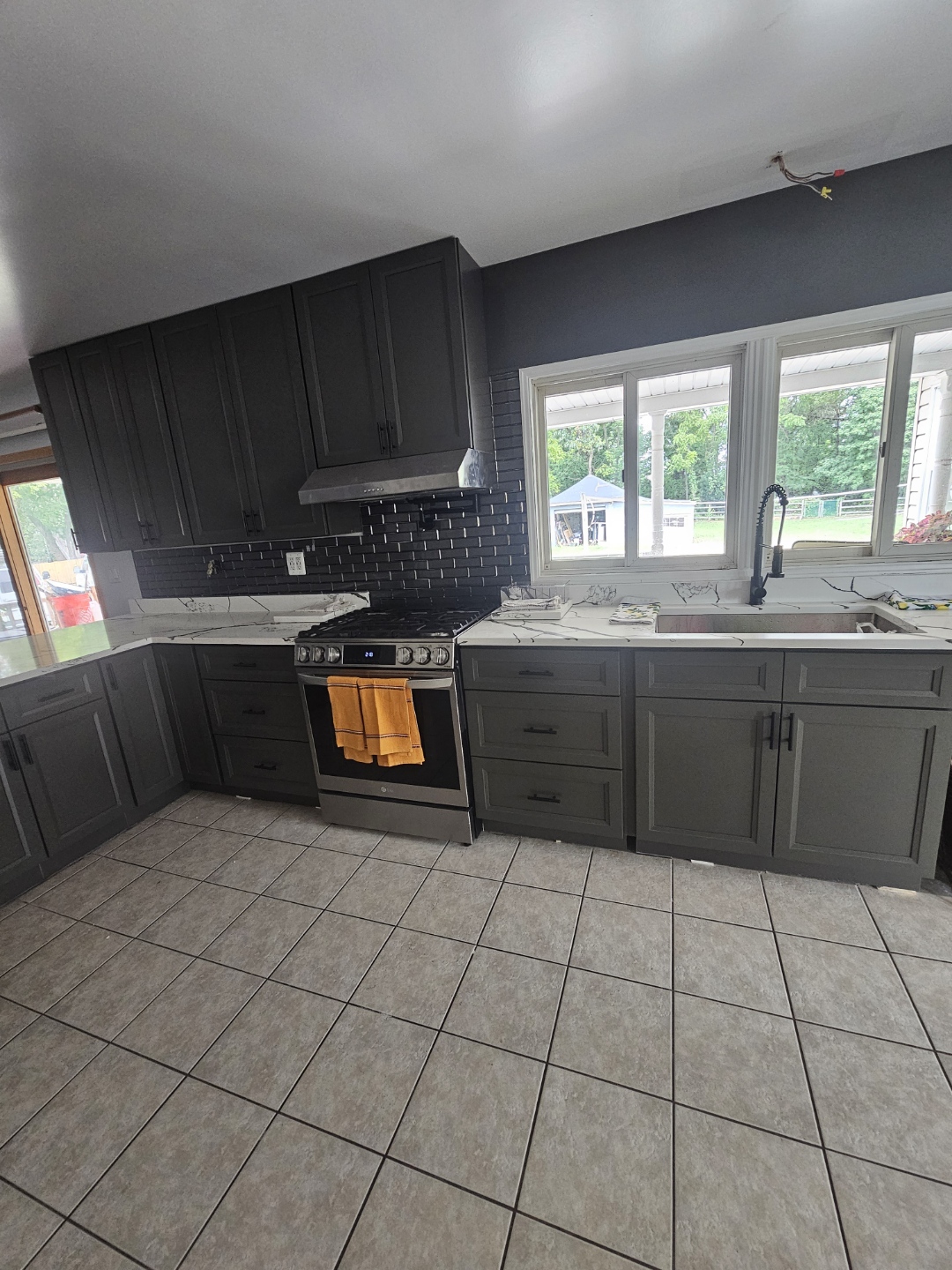 Modern kitchen with dark cabinets, black tile backsplash, and a stove with a yellow towel hanging on it.