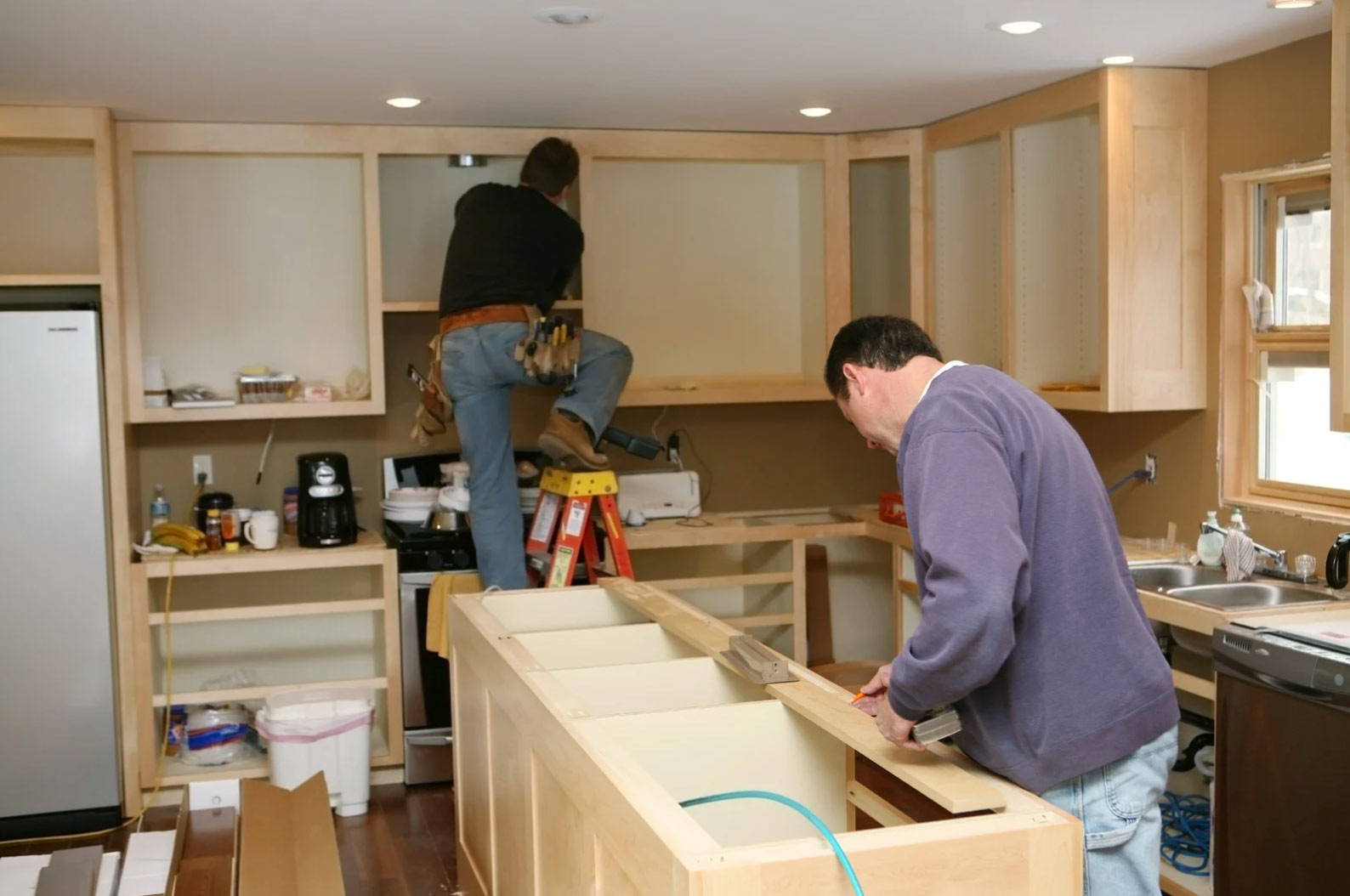 kitchen-1 Two men are installing kitchen cabinets and working on a kitchen remodel with tools and materials.